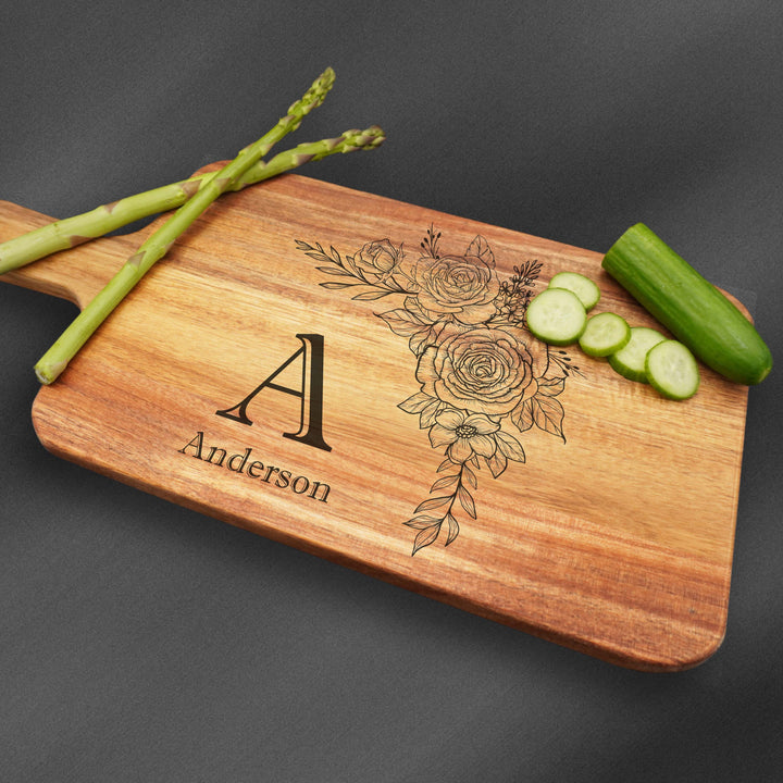 Cutting board with handle and an initial with a last name and flower engraving.